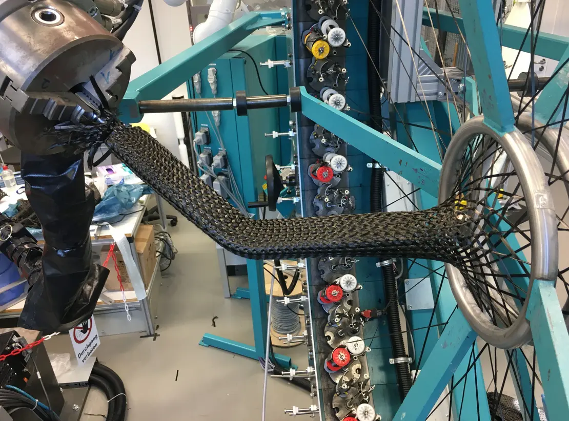 FRP-components with complex geometries? See how to automate manufacturing: Warp yarns turn braid from biaxial into triaxial & nestle it closer to the braiding axis.